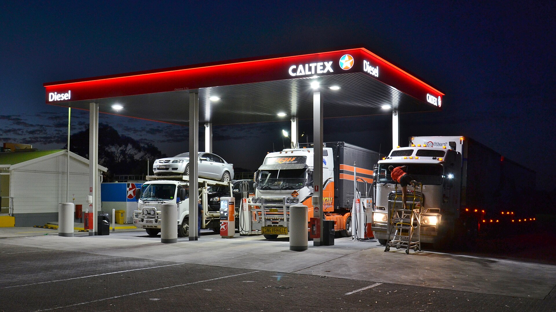 Semi-trucks parked under a lit truck-stop canopy at night