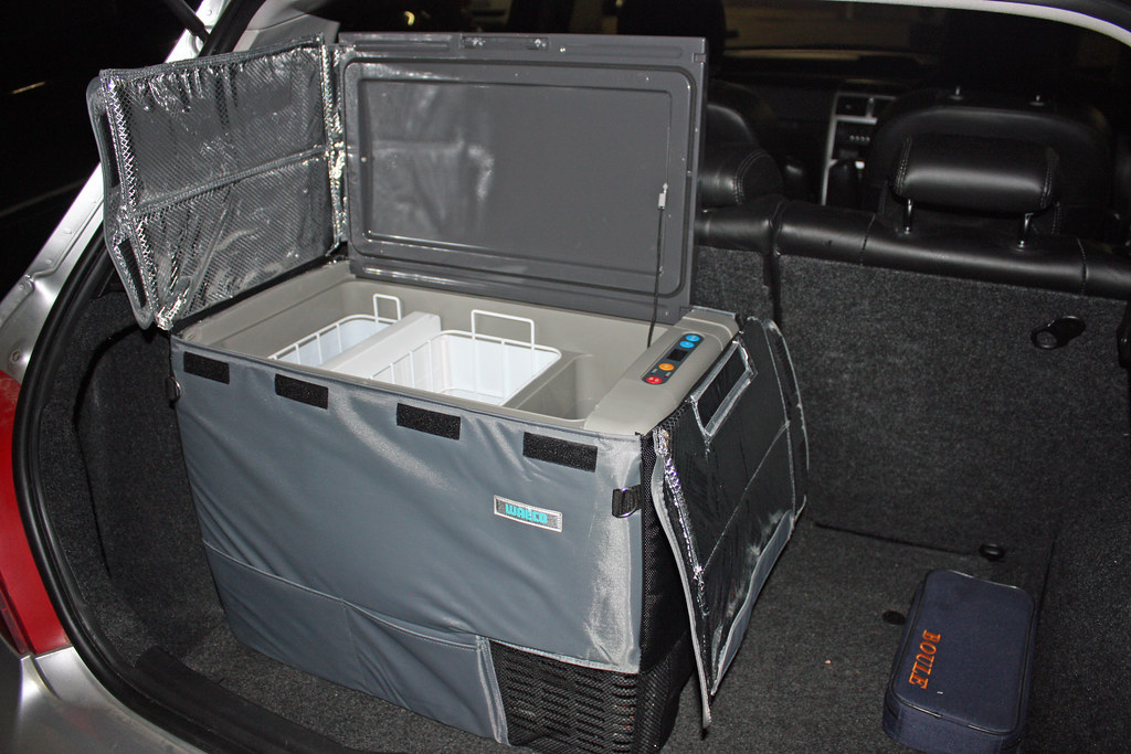 Portable 12V fridge with the lid open, sitting in a car trunk
